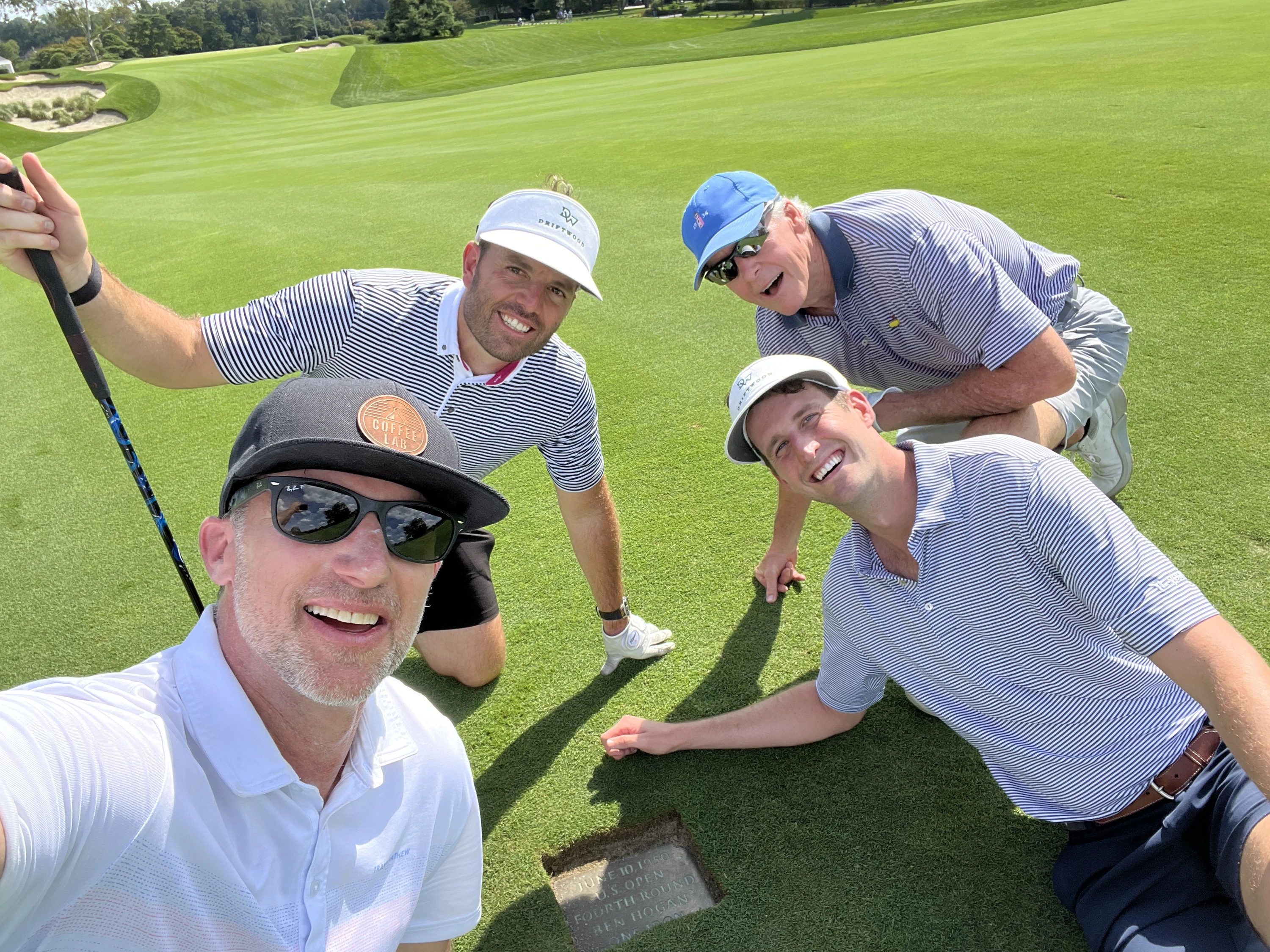 Four golfers gathered around the Ben Hogan 1-iron marker on Merion's 18th hole